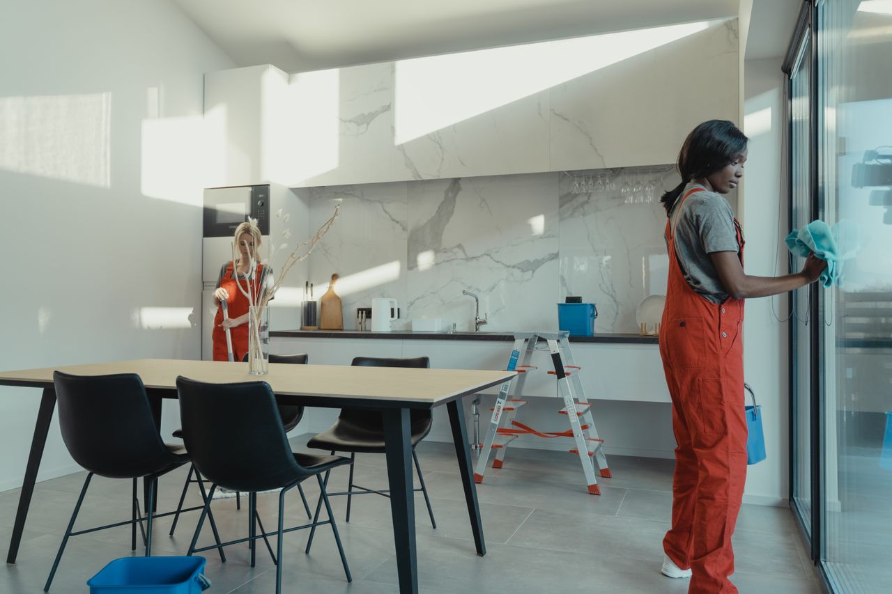 why-choose-us-03 Two women in work clothes cleaning a kitchen with glass doors.
